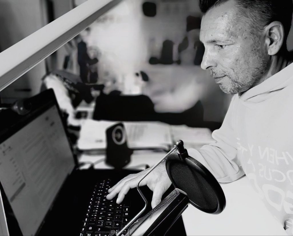 Schreiben Mann arbeitet am Laptop, umgeben von Unterlagen und einer Tasse Kaffee.