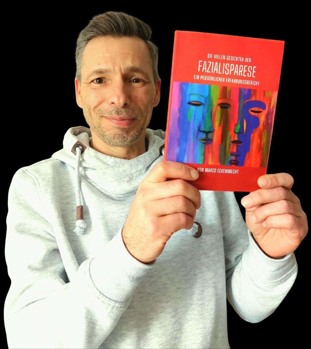Mein erstes Buch Mann hält ein Buch mit bunten Gesichtern auf dem Cover in der Hand.
